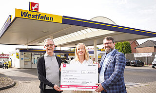 Zwei Männer und eine Frau halten einen Spendenscheck.