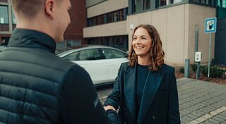Zwei Mitarbeiter:innen auf dem Firmenparkplatz für E-Autos machen Handschlag