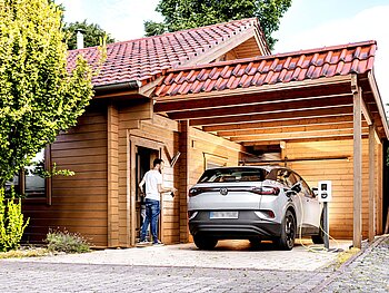 E-Auto Firmenwagen zuhause laden im Carport eines Einfamilienholzhauses