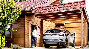 E-Auto Firmenwagen zuhause laden im Carport eines Einfamilienholzhauses