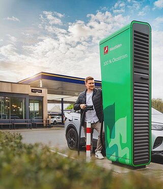 Frau isst Eis am Elektroauto während des Ladevorgangs an einer Westfalen Tankstelle