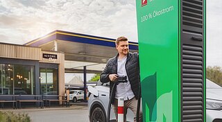 Elektromobilität, Frau ist Eis vor Tankstelle mit Ladestation