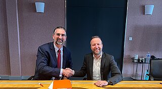 Two men who sitting next to each other, shaking hands