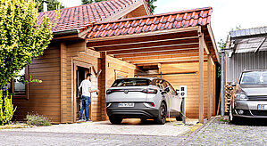 Mann steht im Carport mit E-Auto und Wallbox zuhause