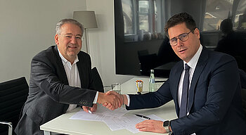 Zwei Männer beim Handschlag an einem weißen Tisch