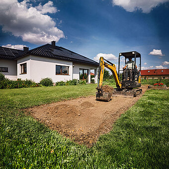 Kleiner Bagger macht Erdreicharbeiten im Garten eines Hauses