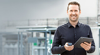Mann auf Betriebsgelände vor Gasflaschen mit Handy und Tablet in der Hand