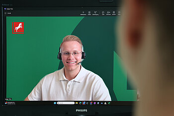 Zwei Personen unterhalten sich per Videotelefonie. Die Person im Vordergrund unscharf am rechten Bildrand sichtbar, die Person auf dem Bildschirm im Fokus.