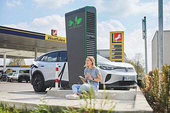 Tankstelle mit Ladestation, Frau sitzt vor Schnellladestation