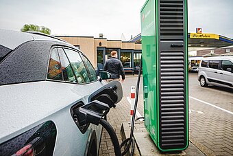 Tankstelle mit Ladestation, Frau sitzt vor Schnellladestation