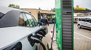 Tankstelle mit Ladestation, Frau sitzt vor Schnellladestation