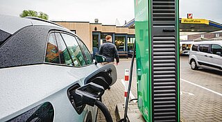 Tankstelle mit Ladestation, Frau sitzt vor Schnellladestation