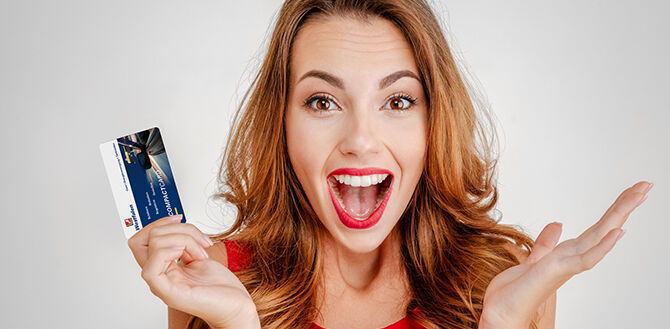 Glückliche Frau mit braunen Haaren hält Westfalen Prepaid-Geschenkkarte in Ihrer Hand.