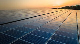 Blue photovoltaic solar panels mounted on building roof for producing clean ecological electricity at sunset. Production of renewable energy concept