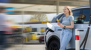 Elektromobilität, Frau ist Eis vor Tankstelle mit Ladestation