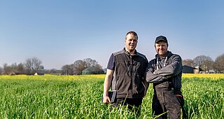 Zwei Landwirte stehen in Arbeitskleidung auf einem Feld