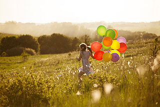 Mädchen rennt mit bunten Ballons auf einer grünen Wiese