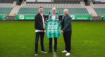 Drei Personen halten ein Trikot in die Kamera