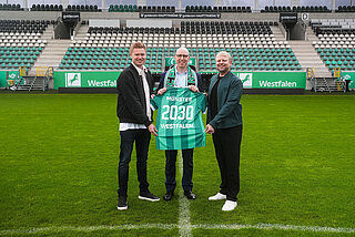 Drei Personen halten ein Trikot in die Kamera