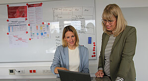 Zwei Frauen an einem Laptop vor einem Whiteboard