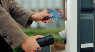 Mitarbeiter hält Westfalen Ladekarte an E-Auto Ladesäule